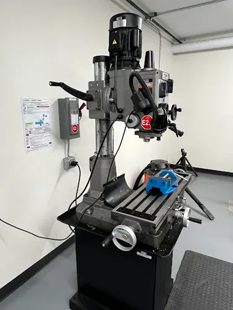 Industrial drill press with an E2 lockout point and a wall-mounted machine-specific placard, the kind of long-lifespan installation aluminum substrate enables