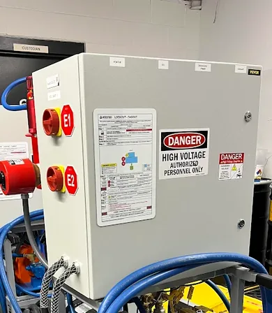 Real installation: high voltage electrical panel with a machine-specific LOTO placard mounted at point of use, E1 and E2 lockout points clearly identified